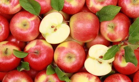 Viele rote Äpfel, einige mit Blättern. Zwei Apfelhälften liegen zwischen den ganzen Äpfeln.