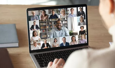 Person vor einem Laptopbildschirm, auf dem viele einzelne Menschen im Portrait zu sehen sind