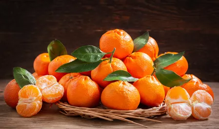 Mandarinen auf einer Schale. Einige sind geschält, andere haben noch Blätter. 