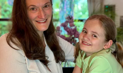 Maren Sturny sitzt seitlich und schaut in die Kamera. Rechts neben ihr sitzt ihre Tochter Sara-Léonie, die einen Sensor am Oberarm trägt. Beide lächeln in die Kamera.