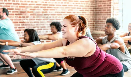 Eine diverse Gruppe Menschen macht Sport. Sie tragen Sportkleidung und machen gerade eine Kniebeuge